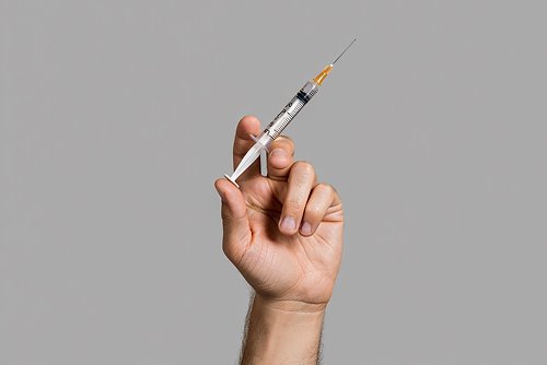 Крупный план руки человека, держащей шприц.